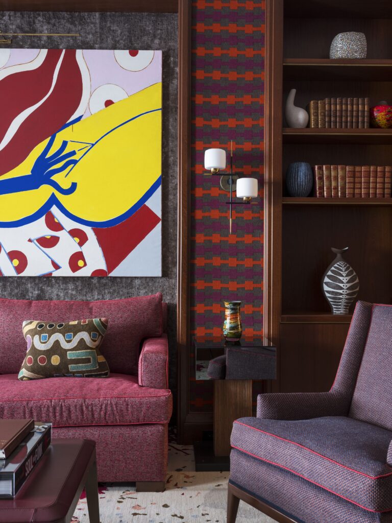 Colorful modern living room with abstract art, red sofa, patterned pillow, and bookshelves filled with decor items.