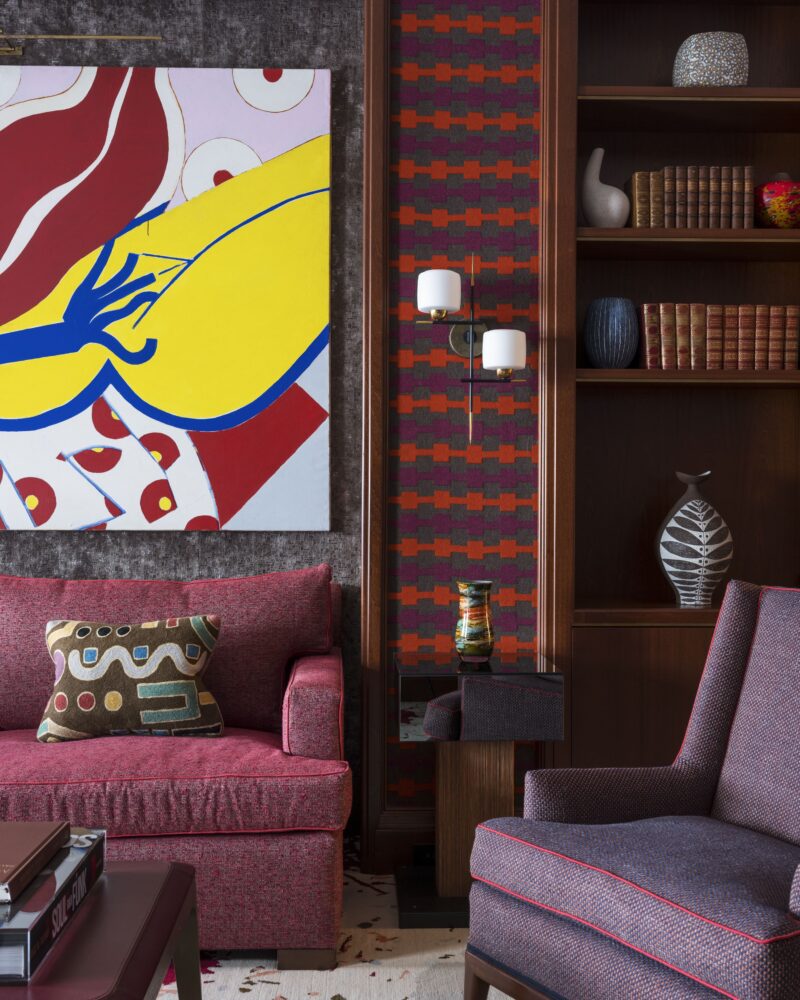 Colorful modern living room with abstract art, red sofa, patterned pillow, and bookshelves filled with decor items.