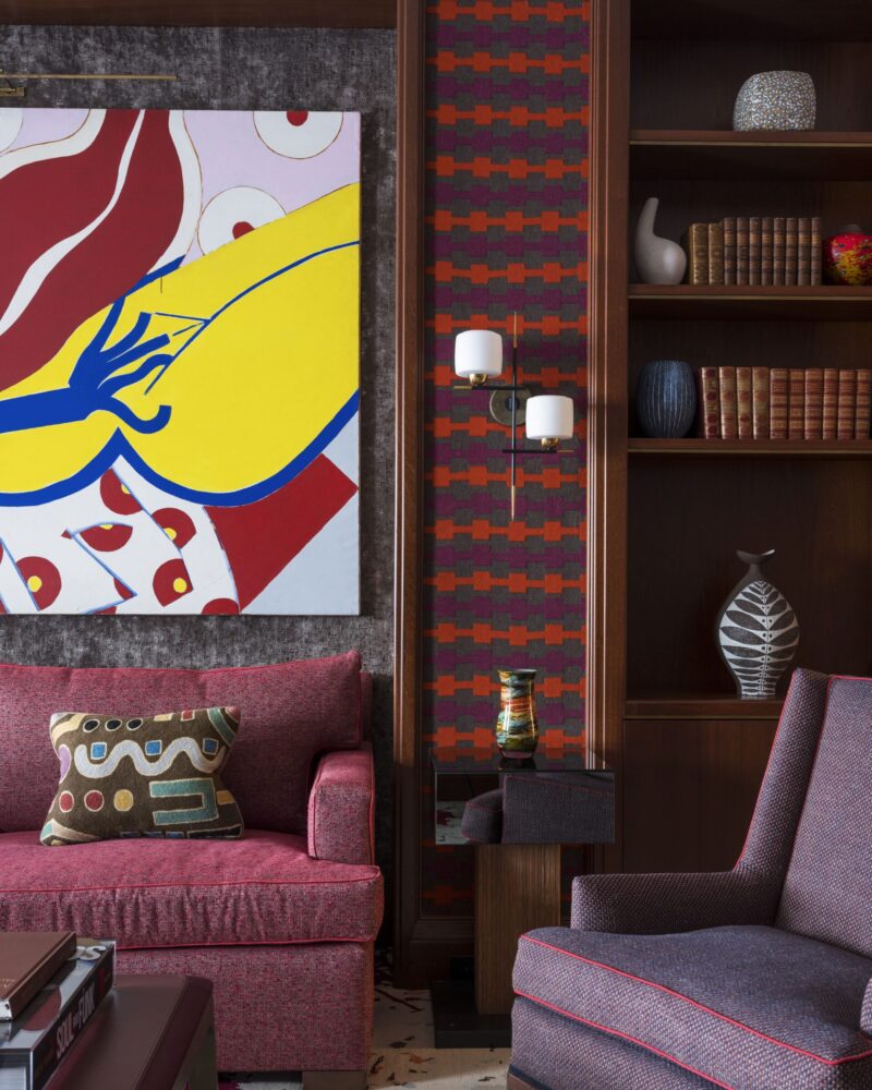 Colorful modern living room with abstract art, red sofa, patterned pillow, and bookshelves filled with decor items.