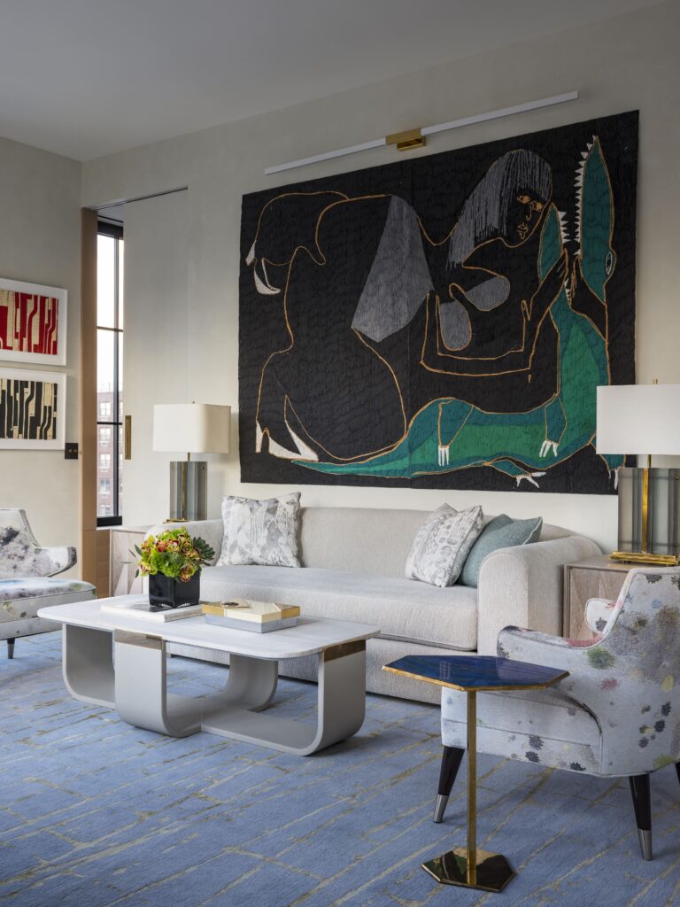 Modern living room with abstract art, light sofa, marble coffee table, and floral armchair on a blue patterned rug.
