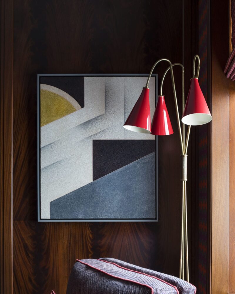 Cozy room with abstract art, red floor lamp, and plush armchair adorned with a decorative pillow and flowers.