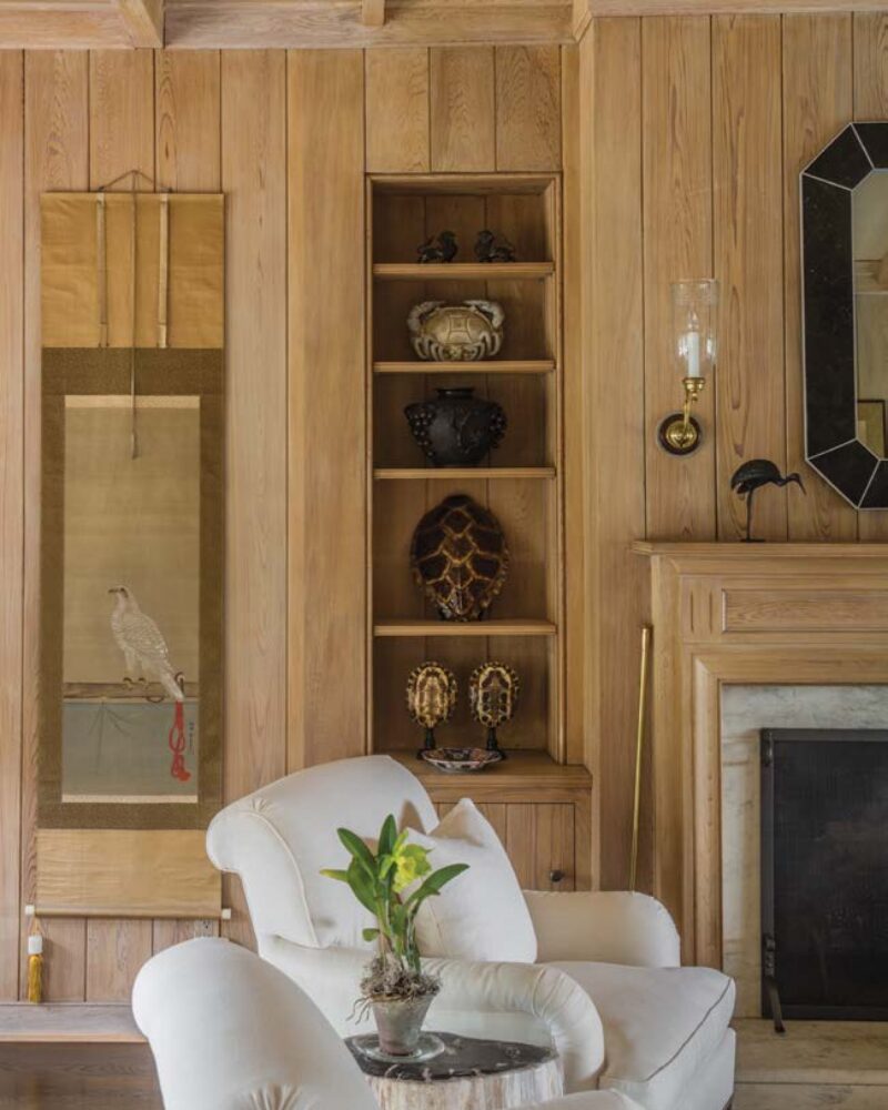 Cozy living room with white armchairs, wooden paneling, decorative shelving, wall art, and a fireplace.