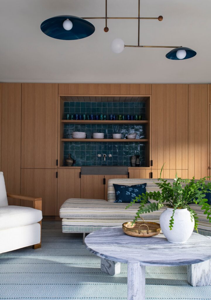 Modern living room with wooden cabinets, blue tile backsplash, striped sofa, and a marble coffee table with a potted plant.