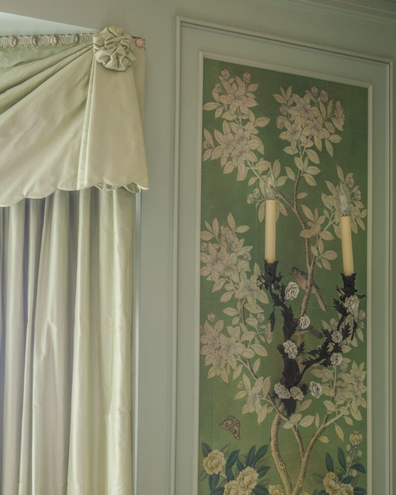 Elegant green floral wallpaper with bird and butterfly design, beside light green drapery with decorative trim.