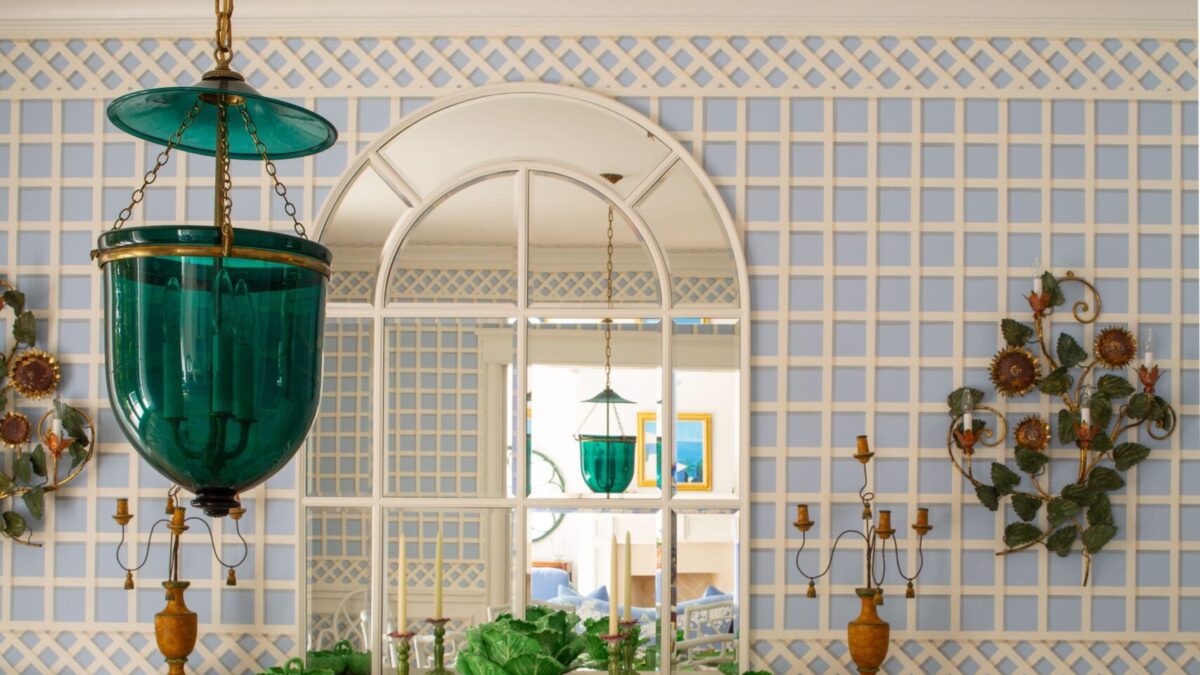 Elegant dining room with green glassware, leaf-patterned plates, and white chairs against a blue lattice wall.