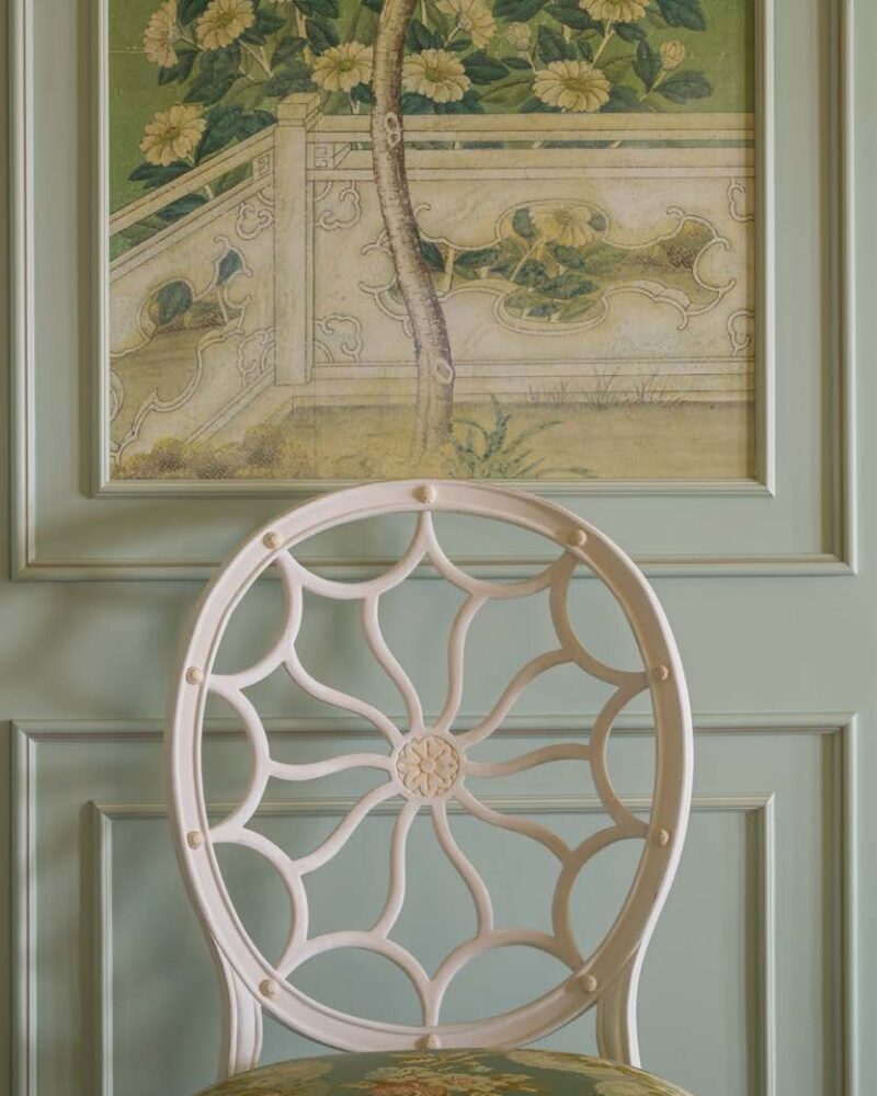 Elegant chair with floral upholstery against a decorative green wall panel featuring a nature-themed painting.