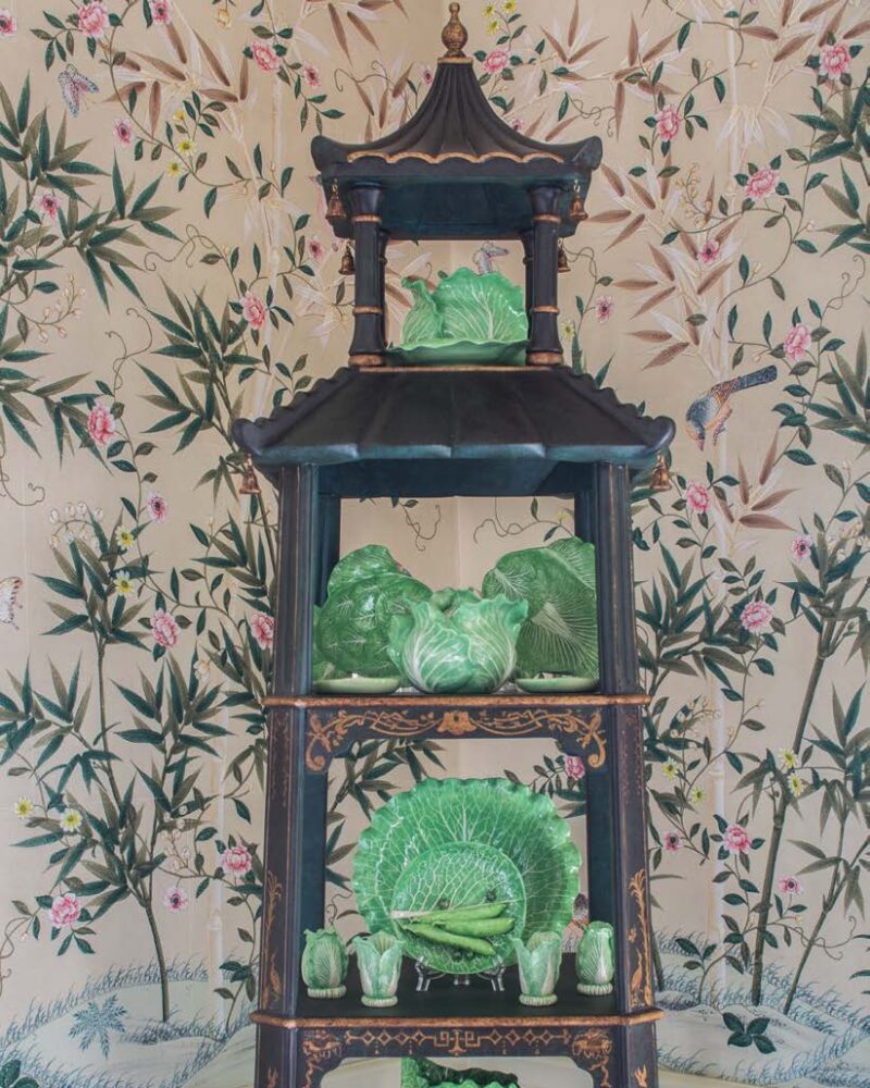 Green cabbage-themed ceramics on a tiered black shelf, set against floral wallpaper with bamboo and pink flowers.