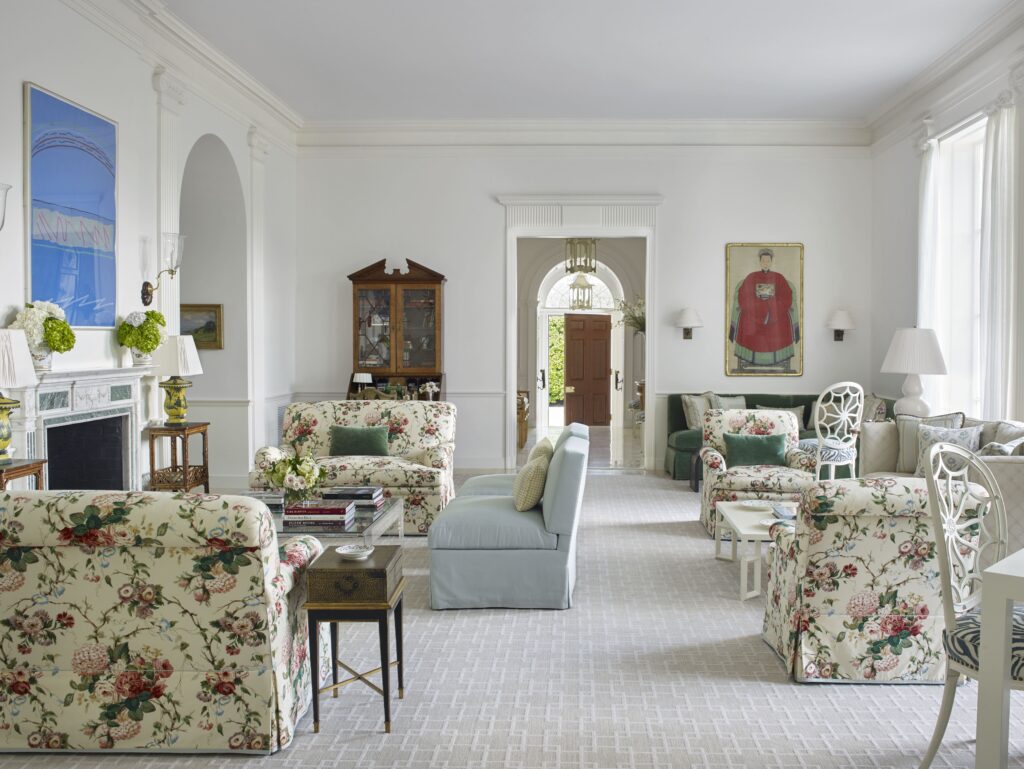 Elegant living room with floral furniture, light blue sofa, and a classic fireplace. Bright, airy space with large windows.