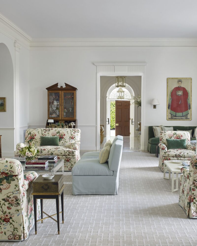 Elegant living room with floral furniture, light blue sofa, and a classic fireplace. Bright, airy space with large windows.