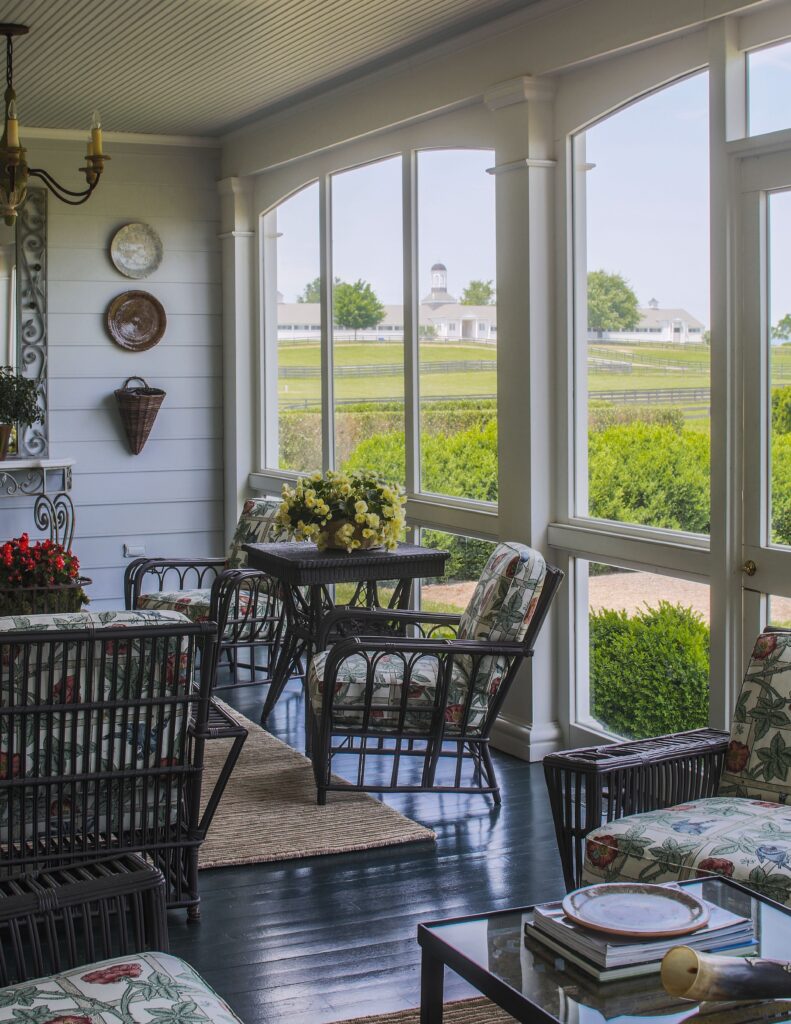 Charming sunroom with floral cushions, wicker furniture, and scenic farm view through large windows.