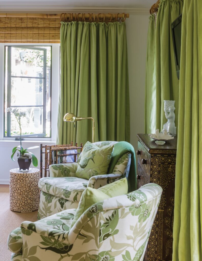 Cozy room with green floral armchairs, matching curtains, bamboo blinds, and a decorative side table near a window.
