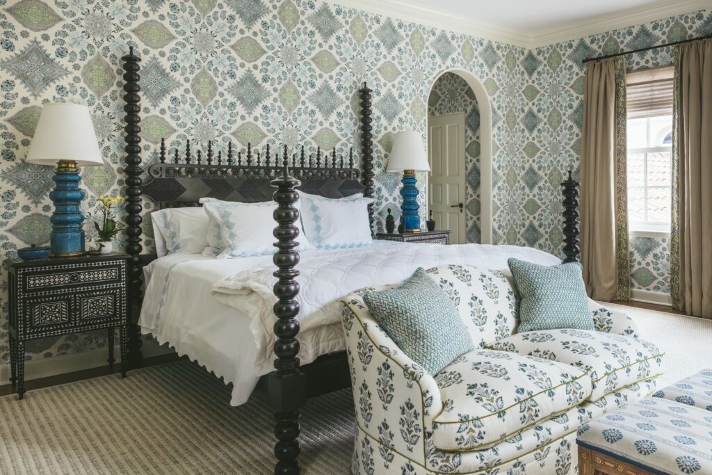 Elegant bedroom with patterned wallpaper, dark wood bed, floral sofa, and blue accents.