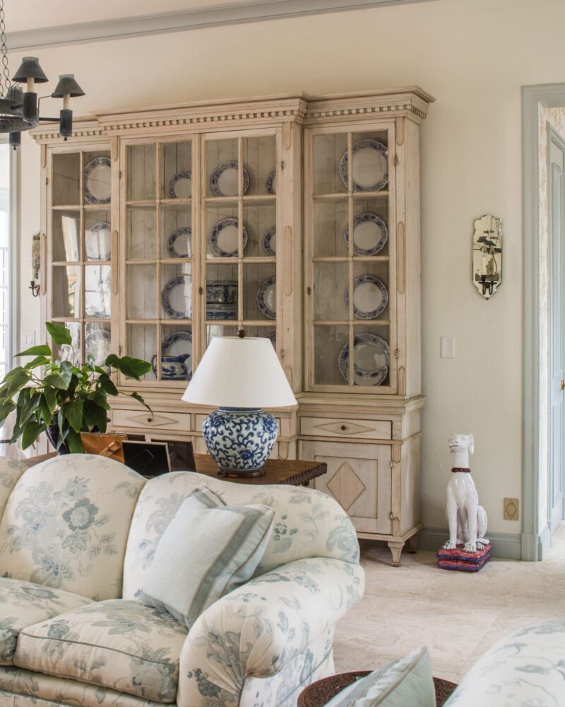 Elegant living room with floral sofa, vintage cabinet, blue-patterned lamp, and ceramic dog statue on stacked books.