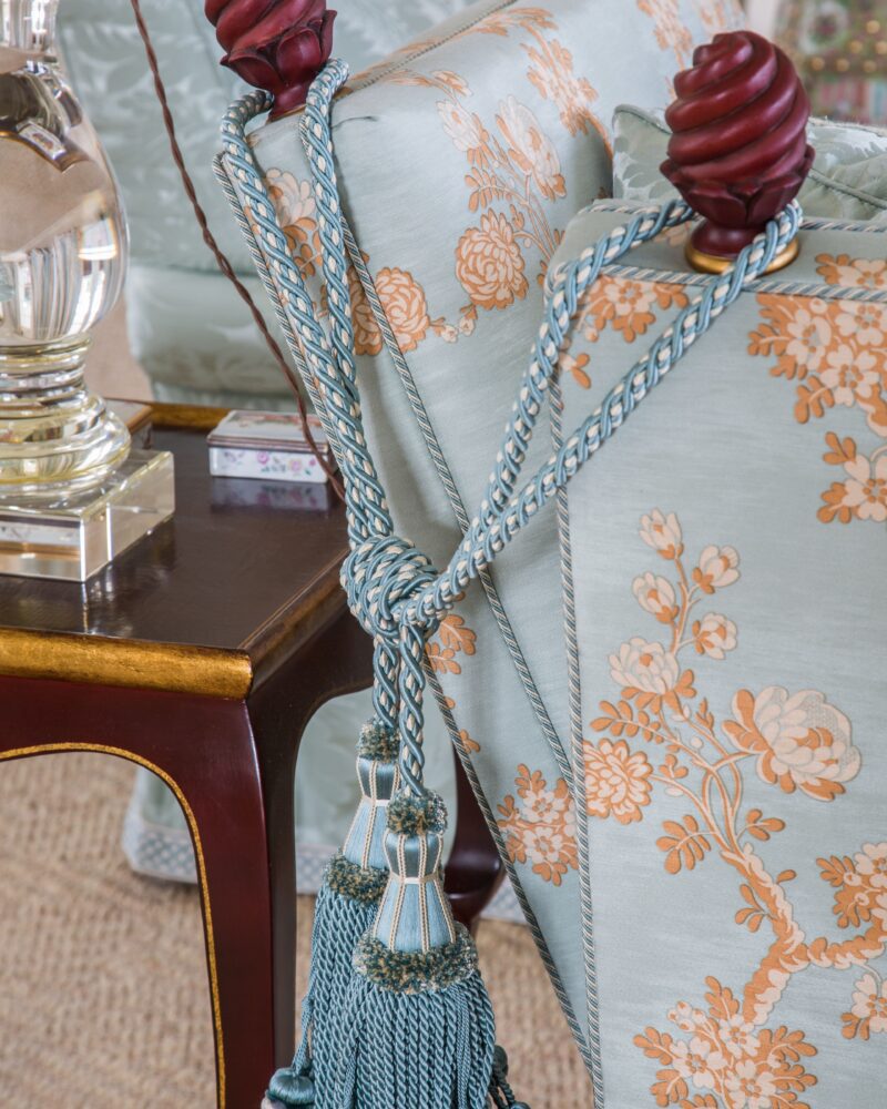 Elegant blue floral upholstery with decorative tassels and a wooden end table.