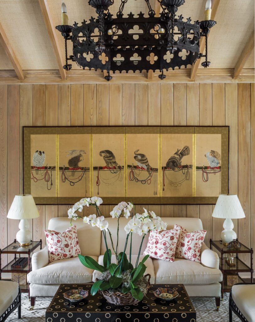 Chic living room with Japanese wall art, plush sofa, floral cushions, orchids, and ornate chandelier.