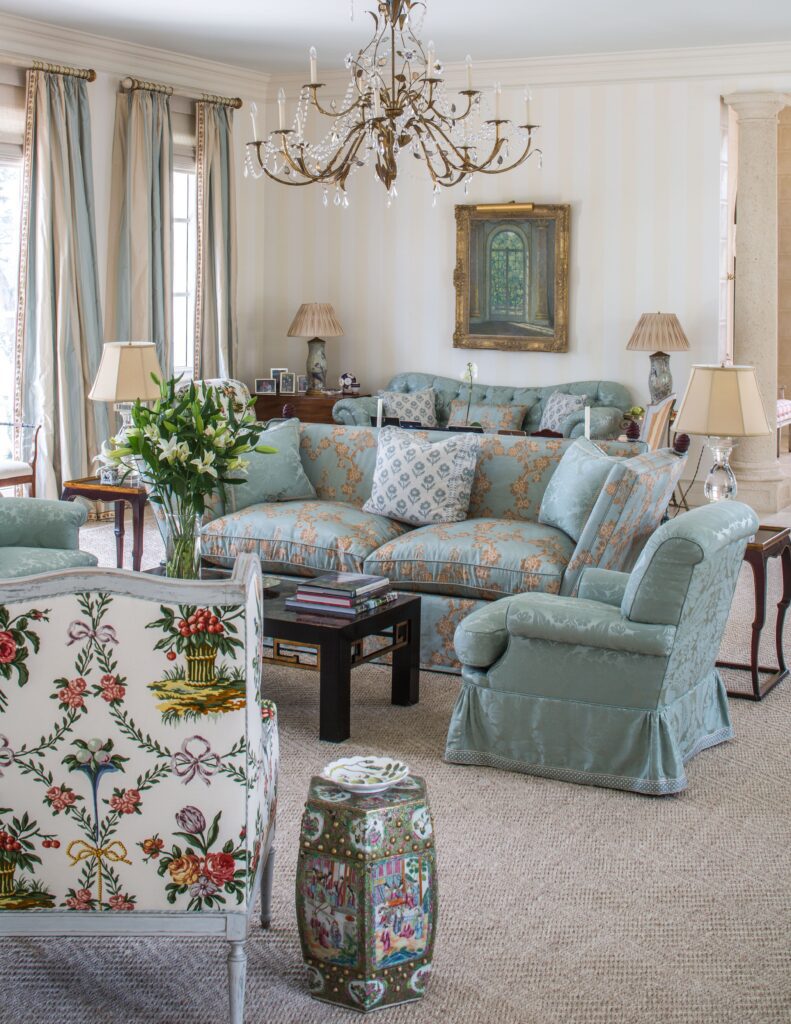 Elegant living room with floral decor, blue upholstery, vintage chandelier, and framed painting, creating a classic ambiance.