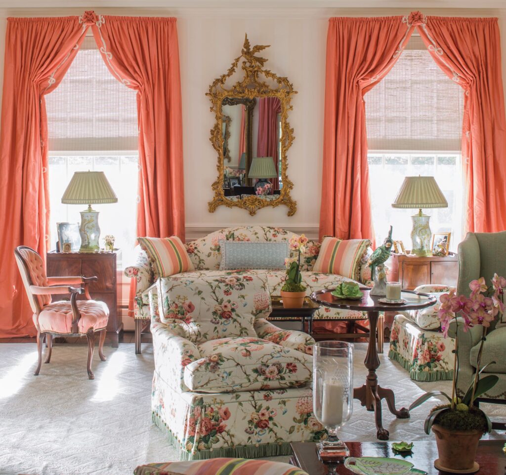 Elegant living room with floral furniture, ornate mirror, coral curtains, and decorative lamps, creating a vintage ambiance.