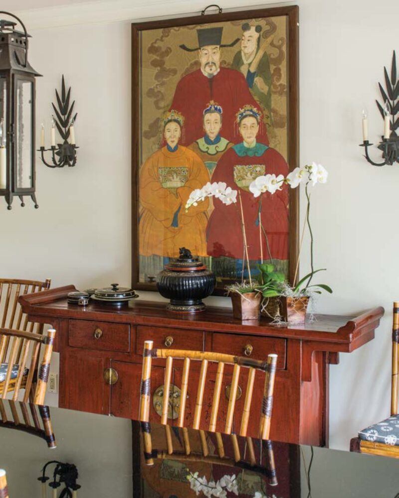 Elegant dining room with a large Chinese painting, wooden furniture, and orchids on a polished table.