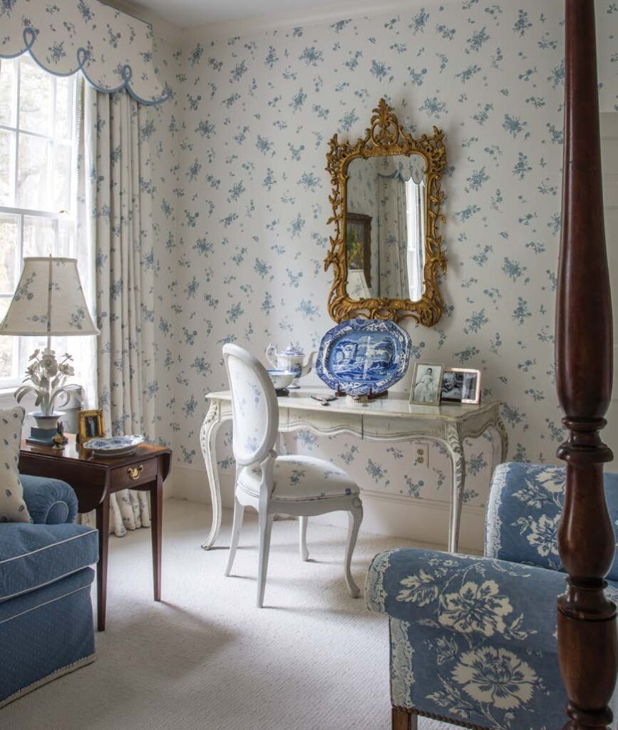 Elegant vintage-style room with floral wallpaper, ornate mirror, and blue accents on furniture and decor.