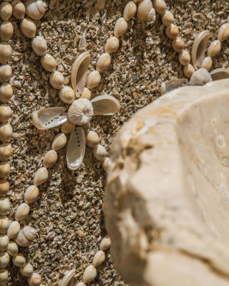 Intricate seashell mosaic design with floral pattern beside a textured stone surface.