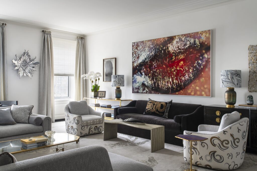 Modern living room with abstract lip art, elegant furniture, and large windows. Neutral tones with floral and metallic accents.