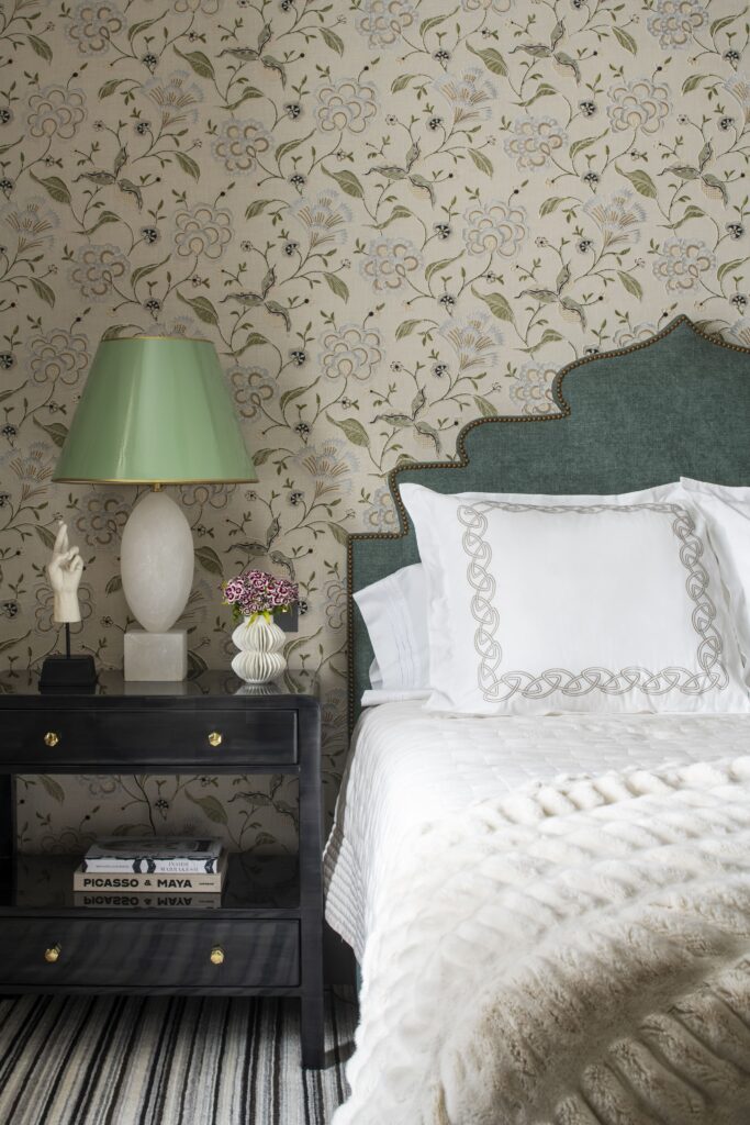 Elegant bedroom with floral wallpaper, green headboard, and stylish nightstand featuring a lamp and decorative items.