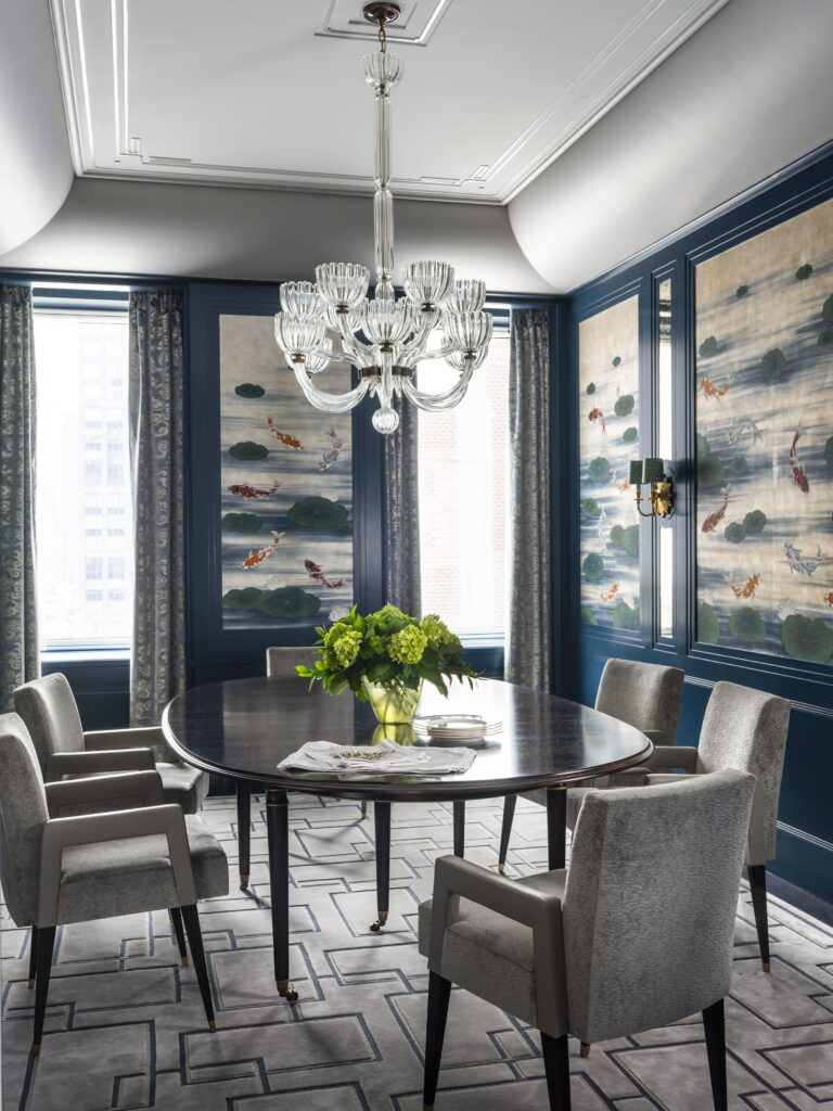 Elegant dining room with glass chandelier, dark wood table, gray chairs, floral wallpaper, and a vase of green flowers.