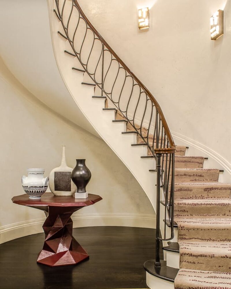 Elegant spiral staircase with decorative table and vases, featuring a modern design and plush carpeted steps.