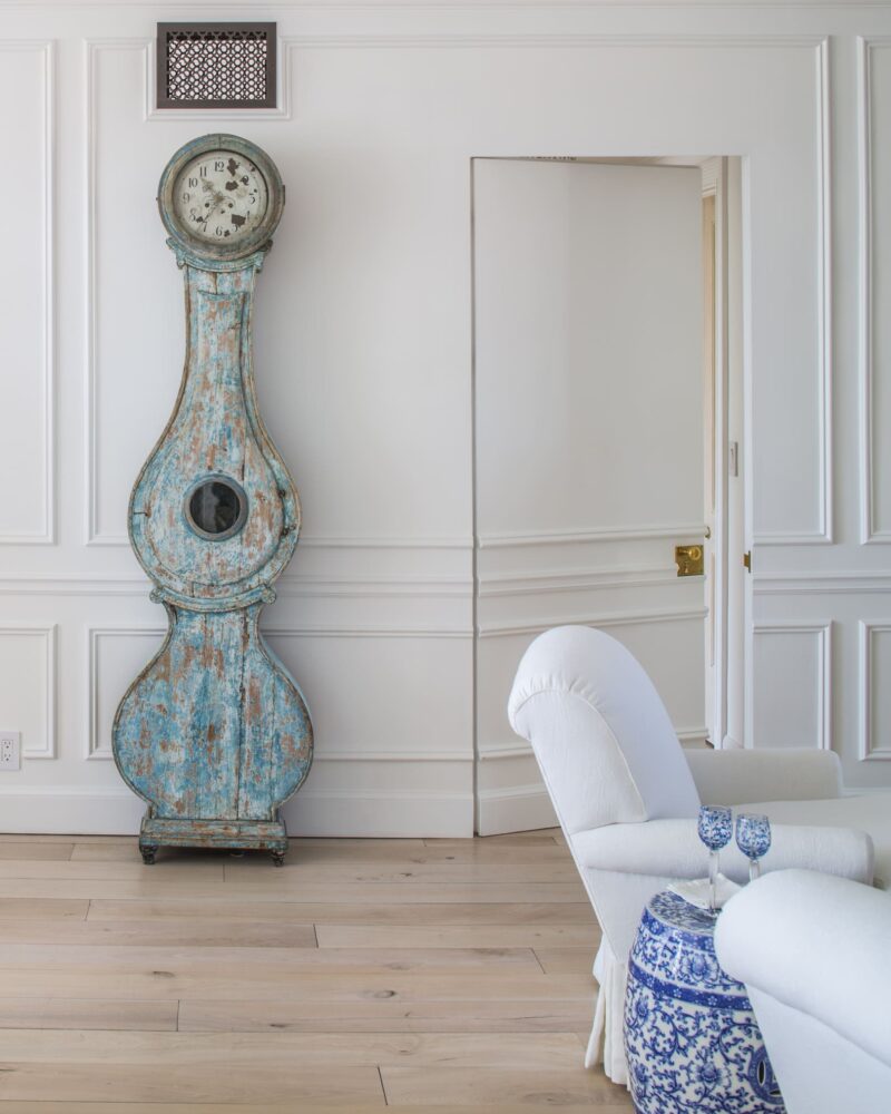 Elegant room with a vintage blue clock, white armchair, and blue-patterned side table on light hardwood flooring.