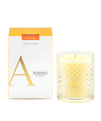 A yellow scented candle in a glass holder next to its white and orange packaging.