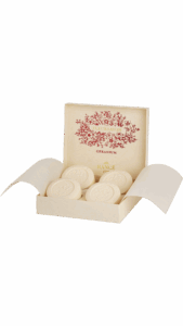 A decorative box contains four round, embossed soap bars labeled "Geranium.