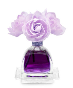 A glass perfume bottle with purple liquid, topped with lavender and rose flowers.