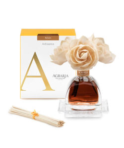 A clear glass fragrance diffuser with cream-colored rose decorations, accompanied by a box and reed sticks.