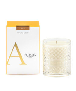 A clear glass candle with a woven pattern beside a yellow and white box labeled "Balsam Perfume Candle.