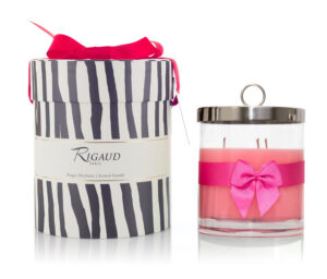 Scented candle in a clear glass container with a pink ribbon, next to a striped gift box.