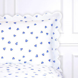 White bedding with blue heart patterns and a scalloped pillow edge against a light background.