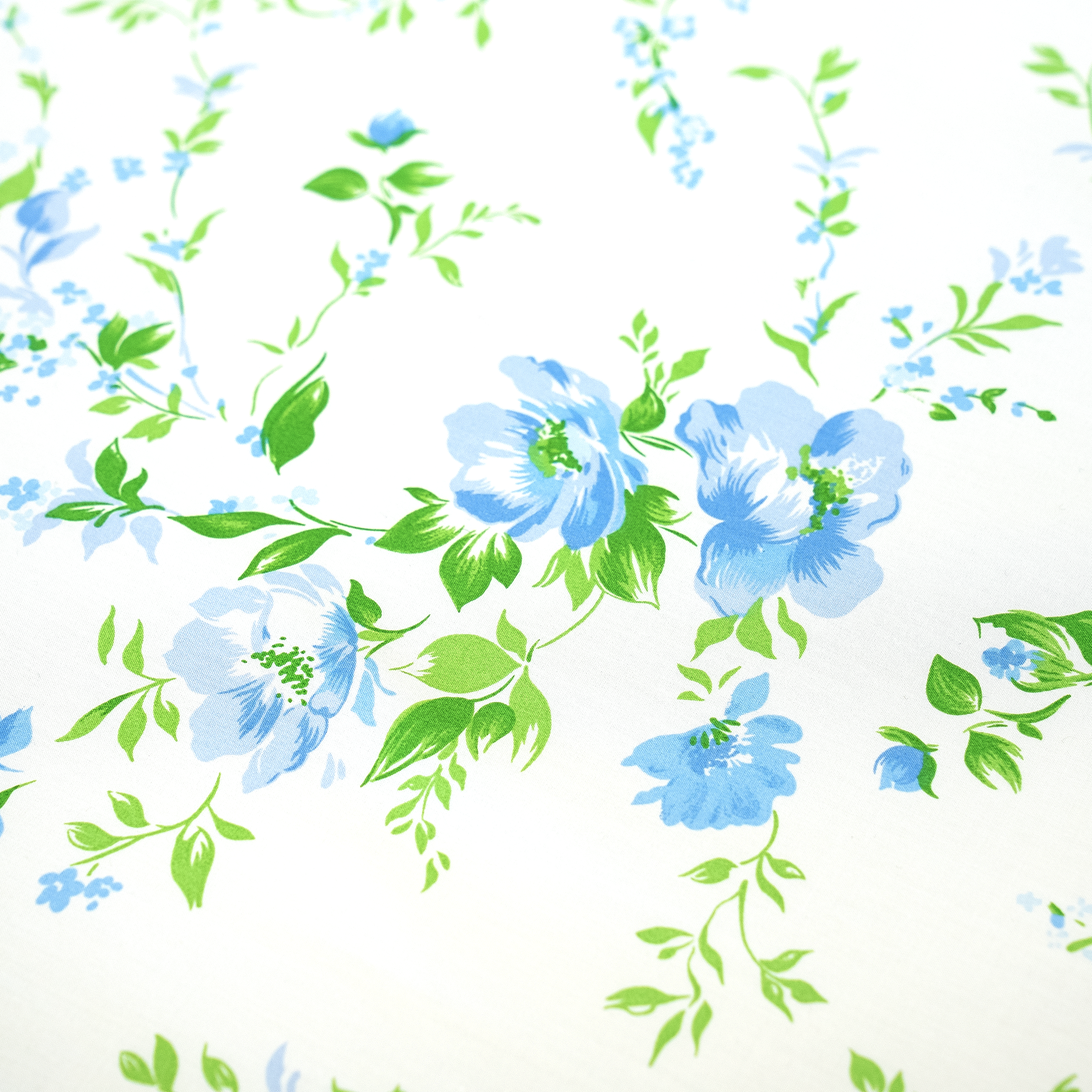 Floral tablecloth featuring blue flowers and green leaves on a white background.