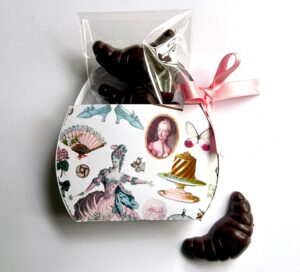 A decorative box features chocolate croissants and images of Marie Antoinette, cakes, and elegant accessories.