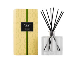 Clear glass reed diffuser with black reeds, next to a yellow box labeled "NEST Grapefruit.
