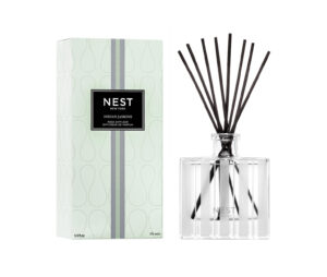Clear glass reed diffuser with black reeds next to a green box labeled "NEST Indian Jasmine.