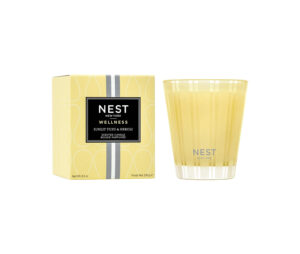 A yellow candle next to its packaging, labeled "Sunlit Yuzu & Neroli" by NEST New York.