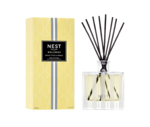 Reed diffuser with black sticks beside a yellow box labeled "NEST Wellness Sunlit Yuzu & Neroli.