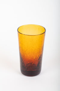 A tall, amber-colored glass with a textured surface, reflecting light.