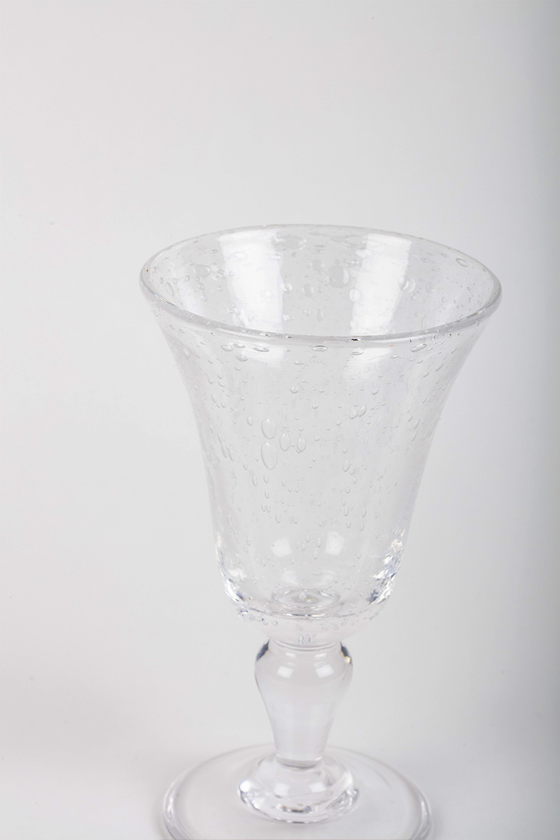 leverre-lignetradi-verre-a-pied-16cm-blanc-2 Clear glass with a flared top and bubbles, standing on a round base.