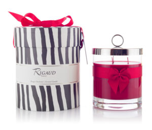 A red scented candle in a glass jar beside a striped gift box with a red ribbon.