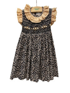Navy dress with floral pattern, ruffled collar, and smocked bodice, hanging on a wooden display.