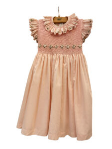 Pink cotton dress with smocked bodice and white daisy embellishments, featuring ruffled sleeves.