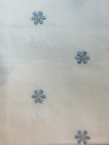 White fabric with blue embroidered daisies featuring yellow centers, scattered across the surface.