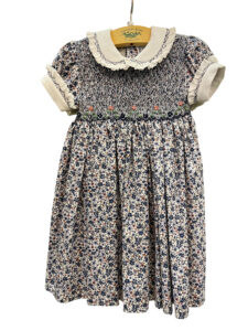 Navy floral dress with rose embroidery and a ruffled collar, hanging on a wooden display.
