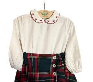 White blouse with a scalloped collar, paired with a red and green plaid skirt featuring buttons.